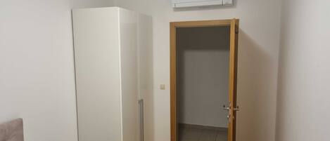 Una habitación con un refrigerador blanco, una puerta de madera y un equipo de aire acondicionado en la pared.