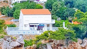 A two-story white building with a red roof, surrounded by greenery and rocky terrain. - Apartments Villa Bella Vista (Orebic)