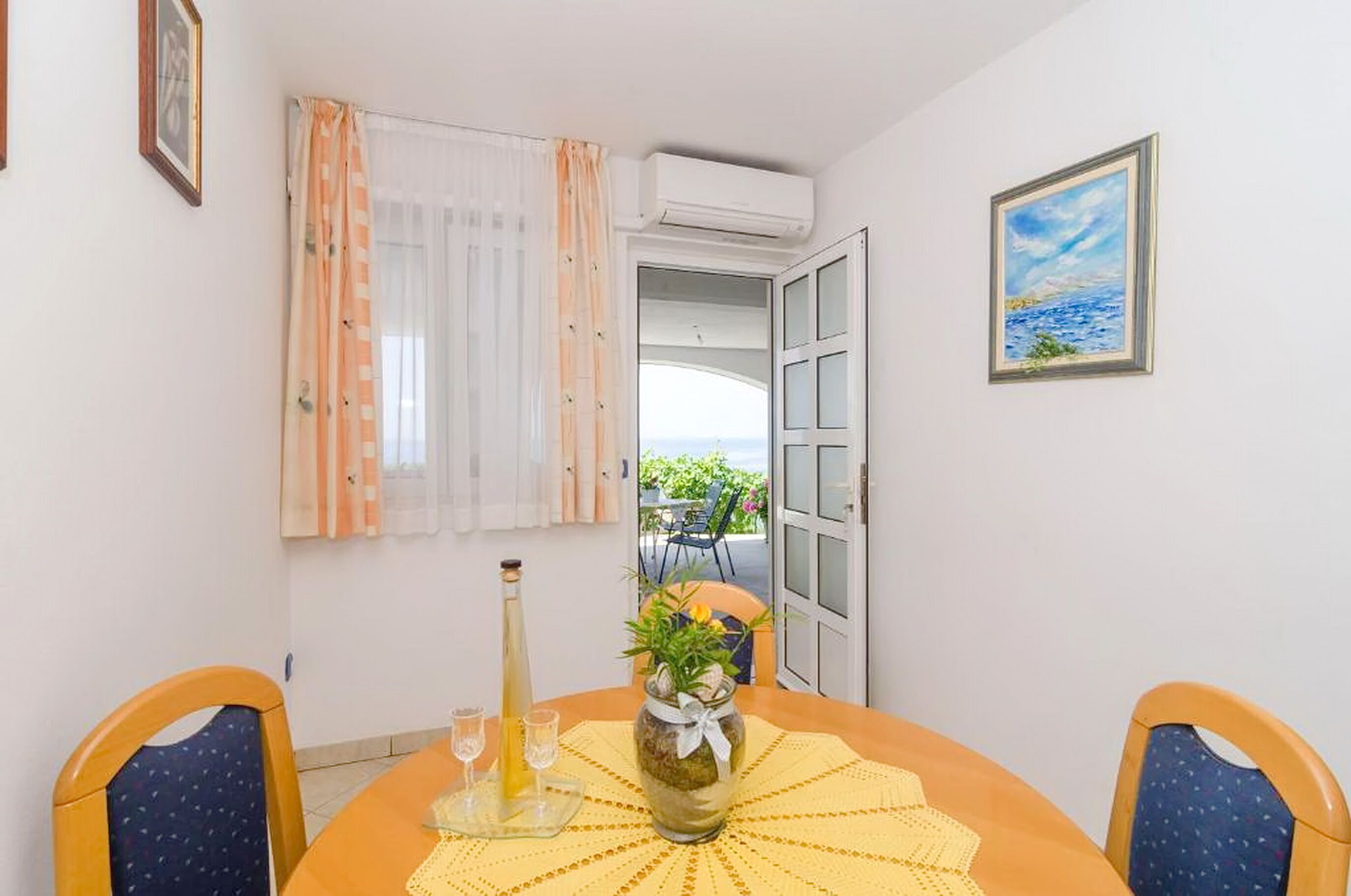 Un coin repas avec une table dressée pour deux personnes, une bouteille et un vase rempli de fleurs.