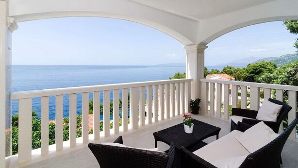 A covered balcony with white railings, wicker furniture, and a view of the sea. - Apartments Villa Bella Vista (Orebic)
