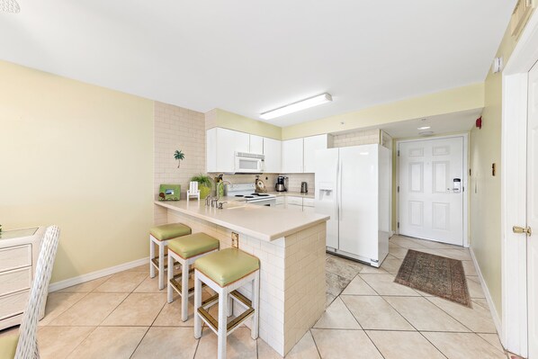 A kitchen with a white island, bar stools, a microwave, and a refrigerator.