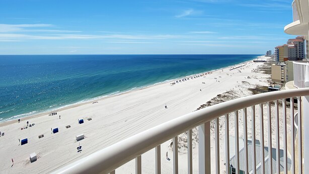 Blick auf einen Strand vom Balkon aus, mit blauem Himmel, Sandstrand und Gebäuden im Hintergrund.