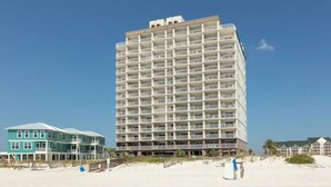 Ein mehrstöckiges Hotel mit Balkonen, gelegen an einem Strand unter blauem Himmel.