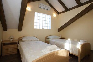 Une chambre avec deux lits simples, des têtes de lit en bois, une fenêtre à carreaux et un appareil de climatisation.