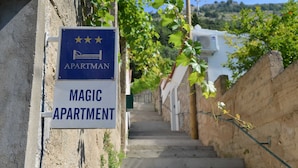 A sign for 'Magic Apartment' with a five-star rating, located on a narrow street with a staircase leading uphill.