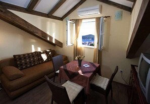 Une pièce chaleureuse avec un canapé marron, une table à manger recouverte d’une nappe rouge et un téléviseur.
