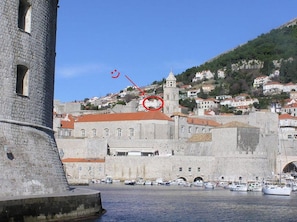 Un bâtiment historique en pierre, doté d’une tour, une église avec un clocher et un port abritant des bateaux.