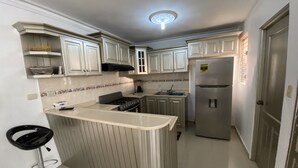 A compact kitchen with white cabinets, a stainless steel refrigerator, and a small island with a sink. - Inviting 3-bedroom Apt in Santo Domingo! (Santo Domingo Norte)