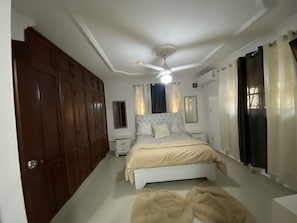 A bedroom with a bed, a ceiling fan, a nightstand, a wardrobe, and a window with curtains. - Cozy 3-bedroom Apartment in Santo Domingo! (Santo Domingo Norte)
