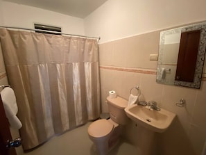 A bathroom with a shower curtain, toilet, sink, and a mirror with a decorative frame. - Cozy 3-bedroom Apartment in Santo Domingo! (Santo Domingo Norte)