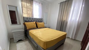 A bedroom with a bed, nightstands, a dresser, a mirror, and curtains.