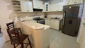 A kitchen with white cabinets, a stove, a sink, and a refrigerator.