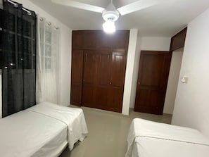 Una habitación con dos camas individuales, un ventilador de techo y un amplio armario de madera.