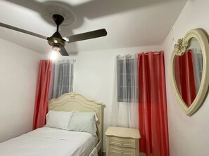 Un dormitorio con cama, mesita de noche, ventilador de techo y espejo.