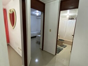 Un pasillo con una cama, un baño con inodoro y ducha, y una cortina roja.