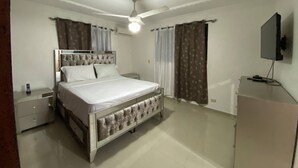 Ein Schlafzimmer mit einem Bett, Nachttischen, einem Fernseher und Vorhängen.