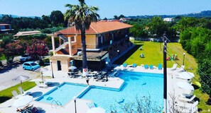 Un edificio de dos pisos con piscina, mobiliario exterior y vistas del paisaje circundante.