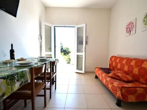 A dining area with a table set for two, a sofa, and a door leading outside.