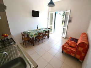 A compact kitchen with a gas stove, a dining table with chairs, and a sofa.