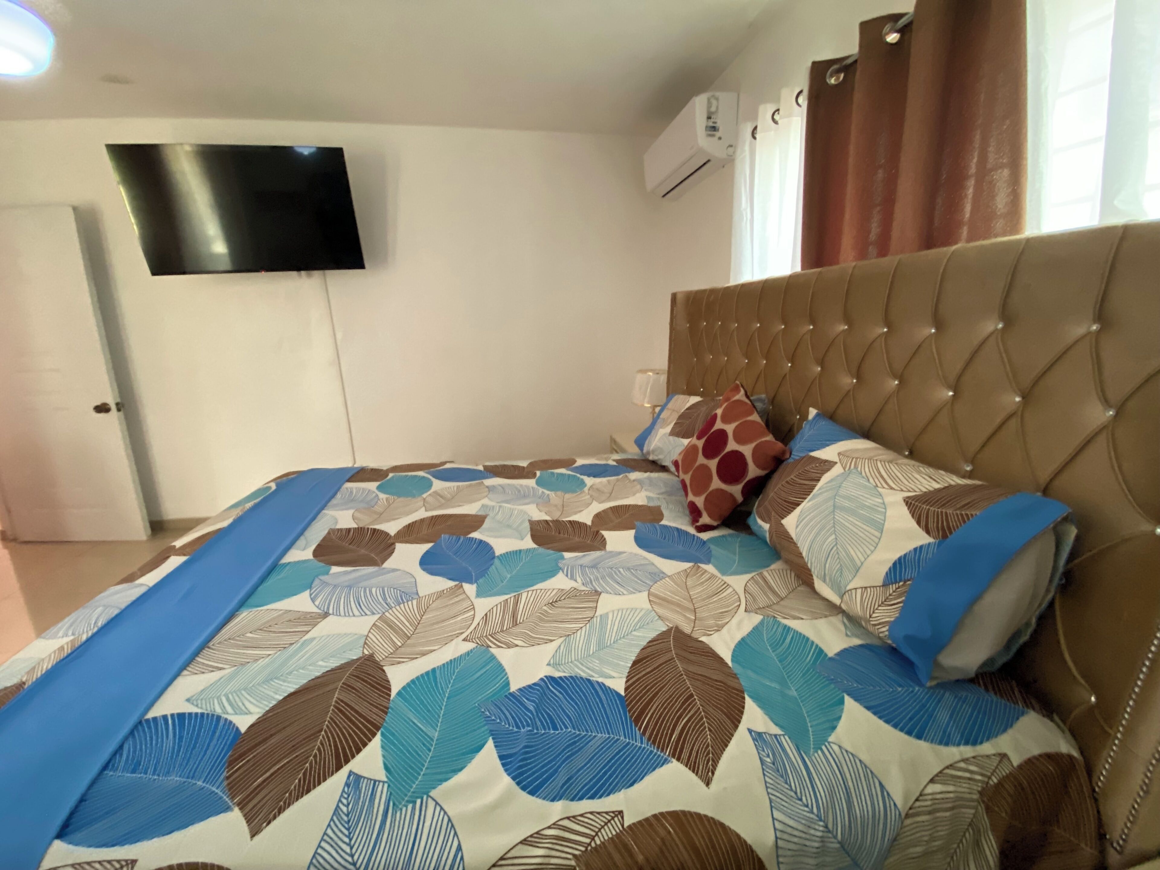 Quarto com cama, televisão na parede e ar condicionado.
