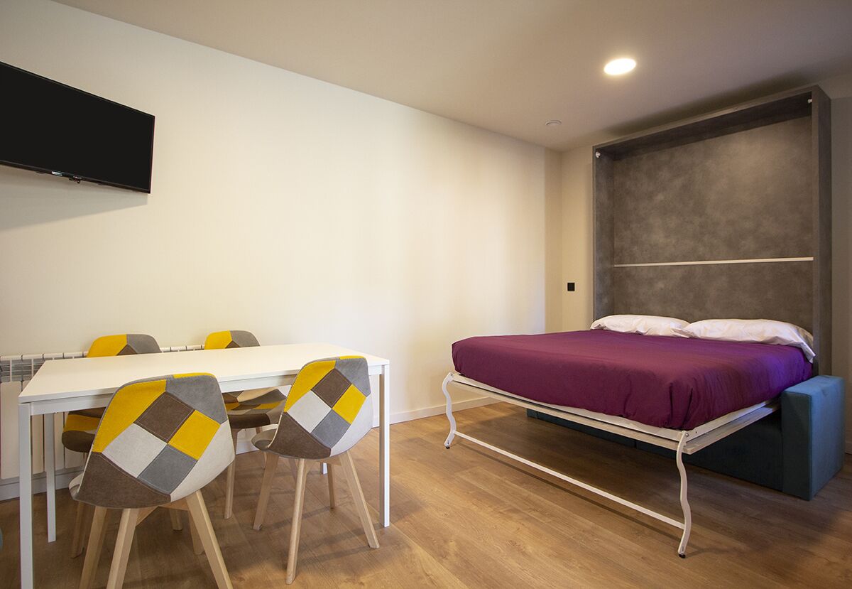 Una habitación pequeña con cama, una mesa blanca y sillas.