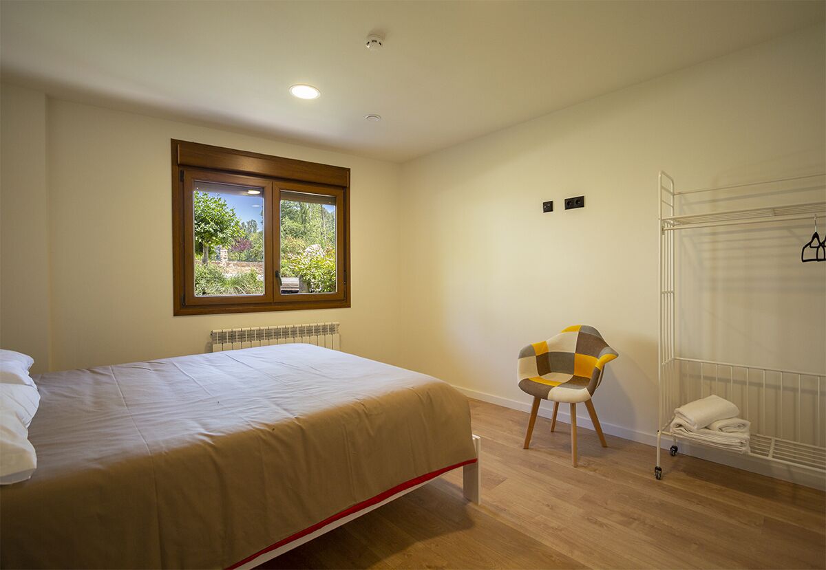 A bedroom with a bed, a chair, a radiator, a window, and a drying rack.