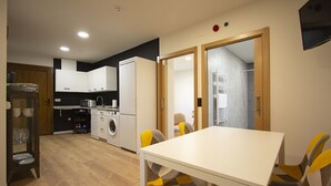 A compact kitchen with modern appliances, a dining area with a white table and chairs, and a visible laundry area. - Accessible Rural Apartments La Rioja (Torrecilla en Cameros)