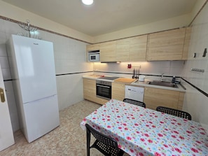 Una cocina compacta con armarios blancos, un microondas, un fregadero y una mesa de comedor con mantel floreado.