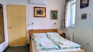 A bedroom with a wooden bed, a door, an air conditioner, and two framed pictures on the wall. - Wine and Relax in Wineregion 1751 (Dunaszentmiklós)