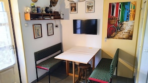 A room with a table, two benches, a TV, wall decorations, and a door with a colorful mural. - Wine and Relax in Wineregion 1751 (Dunaszentmiklós)