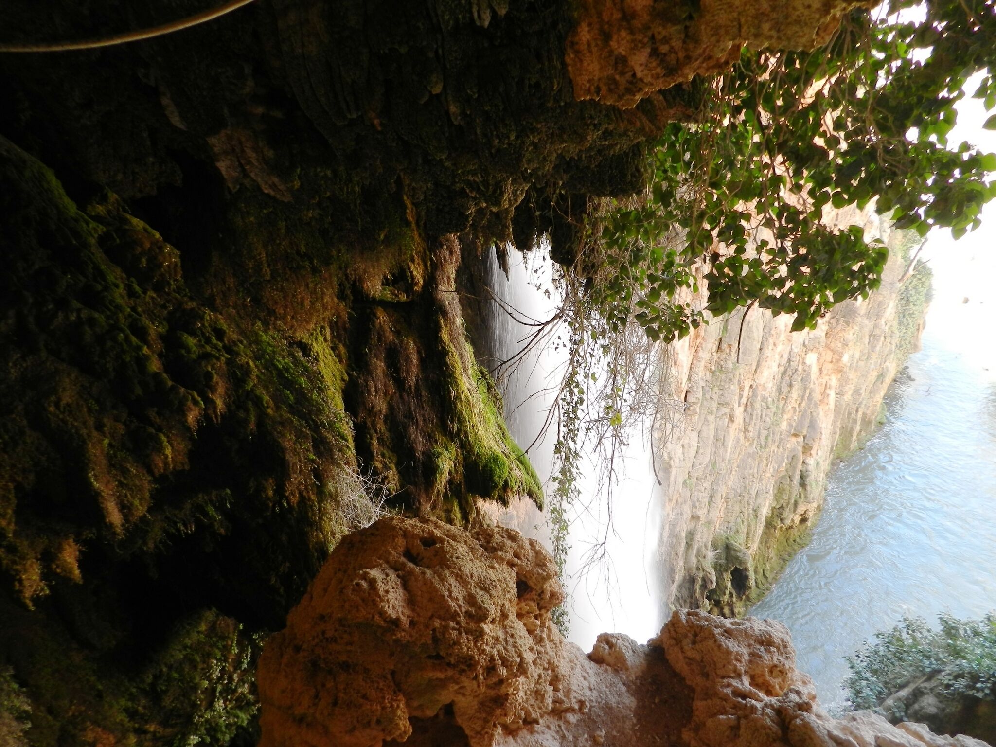 Entrada d'una cova amb una cascada i vista de l'aigua que hi ha a sota.