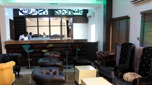 A bar area with stools, a counter, and a seating area with sofas and armchairs. - Room-cubana Suites - Guest Room (Abuja)