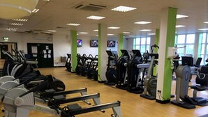 A gym with exercise equipment, wooden flooring, and green pillars. - Room-cubana Suites - Guest Room (Abuja)