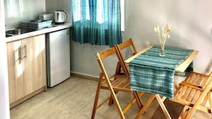 A compact kitchen with wooden cabinets, a stainless steel refrigerator, and a dining area with a table and chairs. - Room-banos Apartments And Swimming Pool (Corfu)