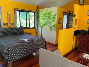 Een kamer met een bed, een klein tafeltje, een stoel, een houten kast en een raam met gordijnen.