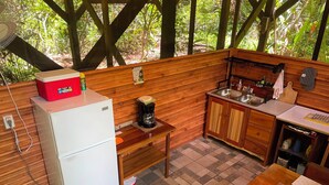 Une cuisine de taille réduite, équipée d’un réfrigérateur, d’une machine à café et de meubles de rangement en bois.