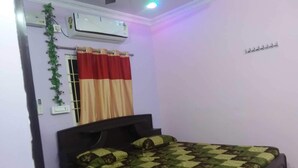 A bedroom with a bed, an air conditioner, a window with red curtains, and a wall-mounted light fixture.