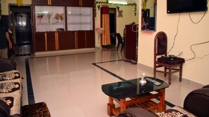 A living room with a glass coffee table, wooden furniture, a television, and a decorative mirror.