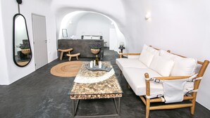 A modern, minimalist room with a curved ceiling, a white sofa, a round coffee table with a stone top, and a wooden chair. - Luxury Cave Villa With Outdoor Hot Tub With Sea Sunset View (Santorini)
