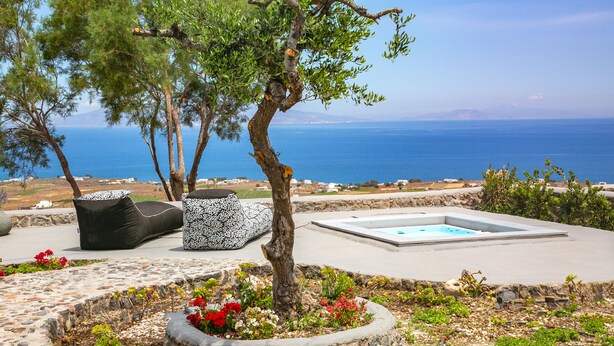 A poolside area with a view of the sea, outdoor seating, and a tree. - Luxury Cave Villa With Outdoor Hot Tub With Sea Sunset View (Santorini)
