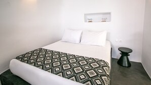 A minimalist bedroom with a bed, a bedside table, and a wall-mounted shelf. - Luxury Cave Villa With Outdoor Hot Tub With Sea Sunset View (Santorini)