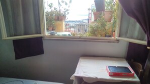 A small room with a bed, a table with a tablet, and a window overlooking a garden. - Room-beautiful Double Room (Taormina)