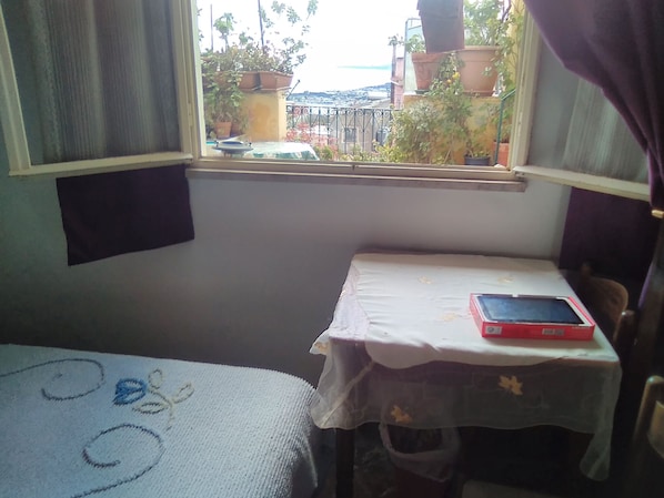 Una habitación pequeña con una cama, una mesa con una tablet, y una ventana que da a un jardín.