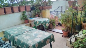 Un espace patio avec deux tables recouvertes de nappes à motifs floraux, entouré de plantes en pot et d’une rambarde en métal.