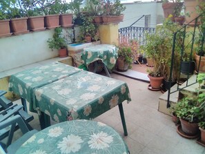 A patio area with two tables covered in floral tablecloths, surrounded by potted plants and a metal railing. - Room-beautiful Double Room (Taormina)