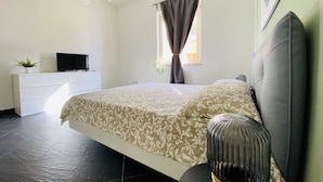 Ein Schlafzimmer mit Bett, Kommode, Fernseher und einem Fenster mit Vorhängen.