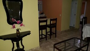A living room with a dining area, a mirror, and a vase with flowers. - Apartahotel Next Nivel - Two Bedroom Apartment (Punta Cana)