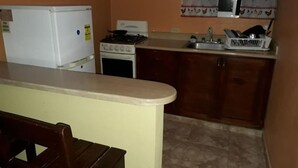 A compact kitchen with a refrigerator, stove, sink, and a small dining area. - Apartahotel Next Nivel - Two Bedroom Apartment (Punta Cana)