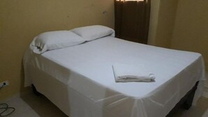 A single bed with white bedding, a folded towel, and a power outlet on the wall. - Apartahotel Next Nivel - Two Bedroom Apartment (Punta Cana)