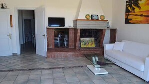 Una sala de estar con chimenea, un sofá blanco y un televisor sobre un mueble.
